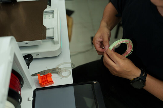 The focus is on the hands of a technician setting up a 3D printer to print a clear white plastic model, using cutting-edge technology and concentrating on specific points within the laboratory.