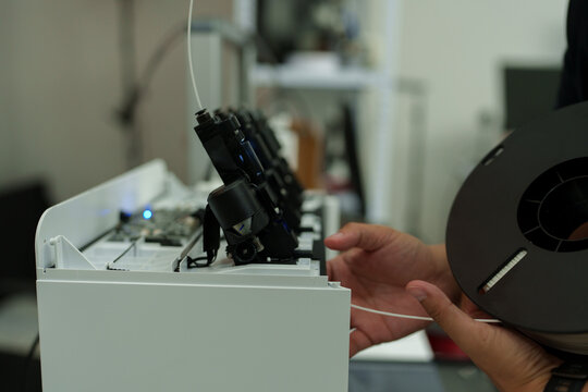 The focus is on the hands of a technician setting up a 3D printer to print a clear white plastic model, using cutting-edge technology and concentrating on specific points within the laboratory.