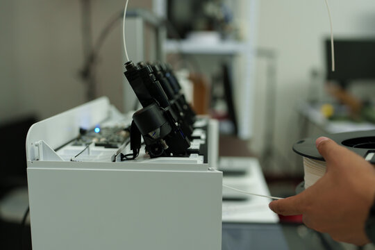 The focus is on the hands of a technician setting up a 3D printer to print a clear white plastic model, using cutting-edge technology and concentrating on specific points within the laboratory.