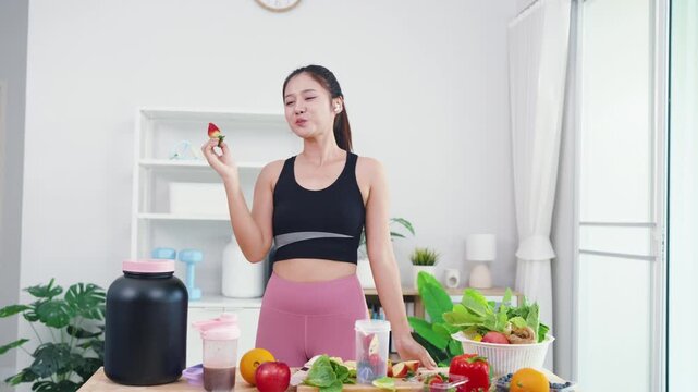 Energetic young female live streaming plant-based diet tutorial using smartphone. Asian wellness vlogger showing fresh vegetables for healthy sports nutrition and vitality.