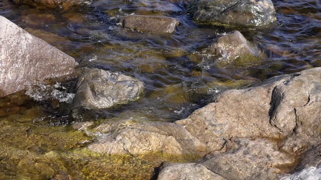 Glistening water flows through a rocky riverbed during a bright afternoon, creating rhythmic splashes and swirls against ancient stones that bring a peaceful sense of nature to the wilderness.