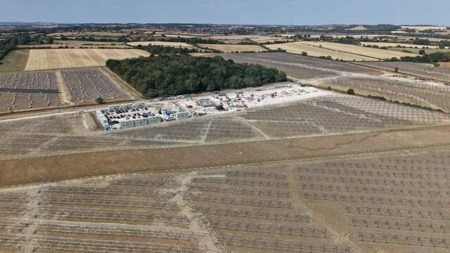 Aerial view of Common Park Solar Farm under construction with rows of metal mounting frames, site containers, and vehicles, surrounded by fields in Sheffield, England, United Kingdom.