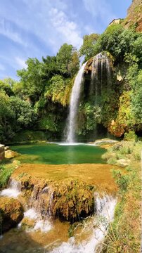 Beautiful waterfall cascading into green natural pool surrounded by lush forest and rocks. Salles la source, Aveyron in France