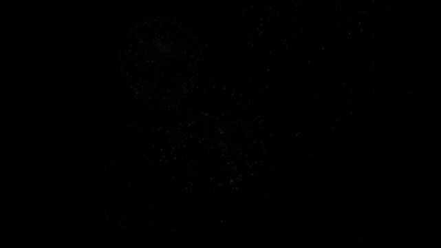 Fireworks sparks flicker faintly in total darkness against a solid black background creating abstract night texture.
