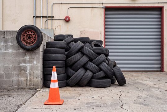 Pile of used car tires next to an industrial building with a traffic cone