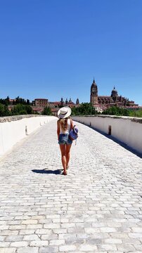 woman walking on roman bridge towards salamanca cathedral in spain