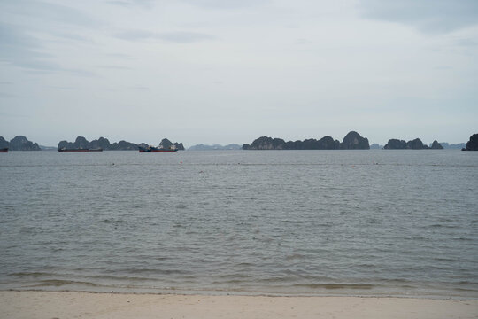 Serene seascape featuring rocky islands and distant ships under a cloudy sky.