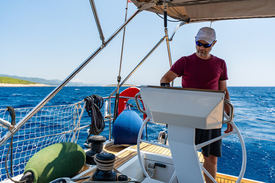 Experienced sailor steering a sailing yacht during an offshore passage at sea. Seamanship, navigation skills, confident boat handling and active cruising lifestyle.