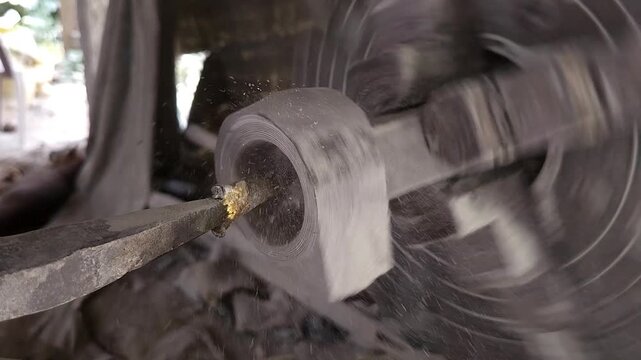 Slow-motion horizontal footage of an Indian artisan shaping a granite stone utensil on a rotating lathe machine. The spinning stone is carefully worked with cutting tools to create a rounded form