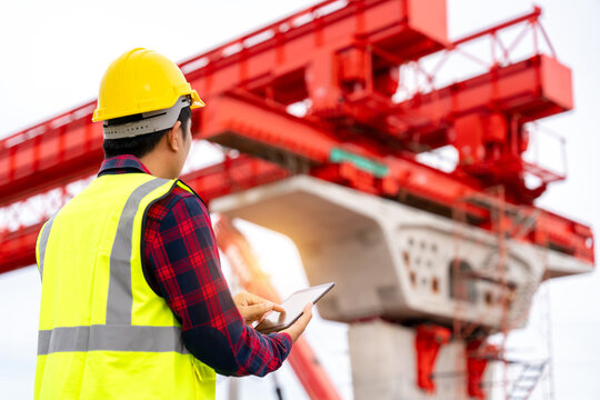 A construction engineer using a tablet to inspect a bridge project with launching gantry, representing civil engineering, construction technology, safety and infrastructure development.