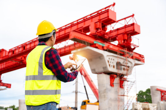 A construction engineer using a digital tablet to inspect a bridge project with launching gantry, representing civil engineering, construction technology and infrastructure development.