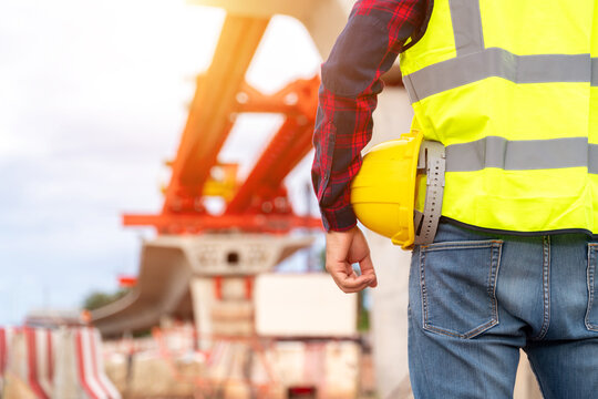 Close up of Construction worker holding a safety helmet at a bridge construction site with copy space, representing civil engineering, workplace safety and infrastructure development.