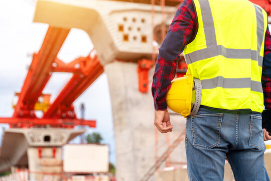 Close up of Construction engineer holding a safety helmet at a bridge construction site, representing civil engineering, worker safety, infrastructure development and project management.