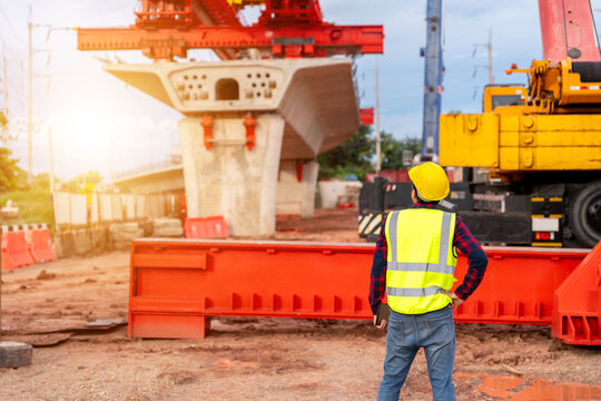 A construction engineer supervising a large bridge project with heavy crane and concrete structure, representing civil engineering, safety, leadership and infrastructure development.