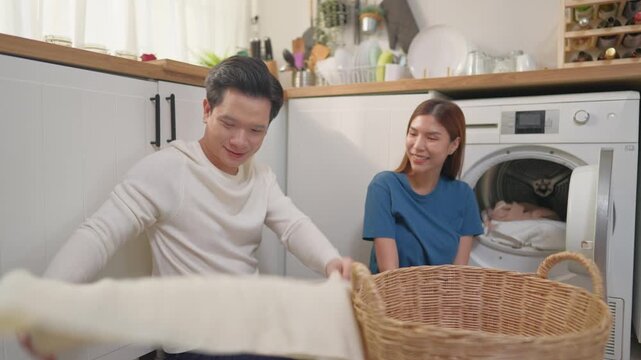 Attractive couple put dirty clothes to washing machine in house together. 