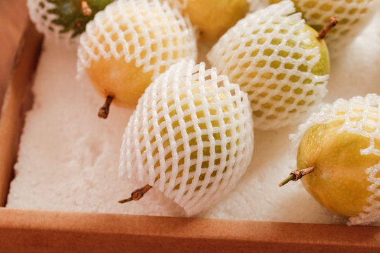 Golden pears in protective foam netting arranged in wooden crate for fresh fruit packaging and transport