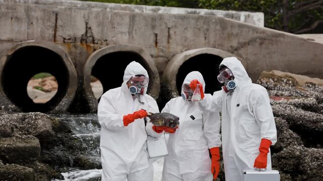 Three scientists in hazmat suits collect water samples near a polluted coastal outfall, wearing respirators and gloves amid foamy wastewater and barnacle-covered drainage pipes.