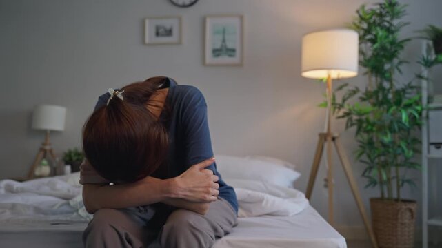 Depressed Asian young woman feel upset while sitting on bed in bedroom. 