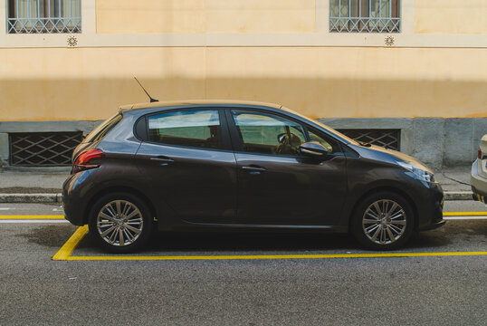 Dark grey Peugeot 208 subcompact car parked between yellow lines on asphalt in a European city