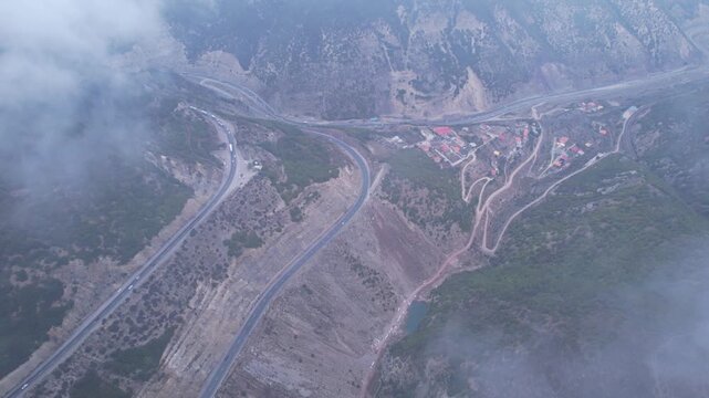 Foggy mountain highway curves through misty hills with vehicles on asphalt road under cloudy sky for travel infrastructure adventure nature landscape drone photography footage high resolution stock