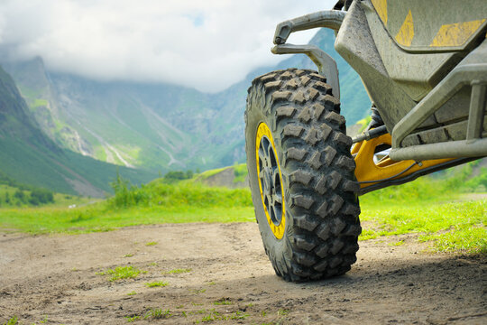 Close up of a yellow dirty offroad UTV buggy car parked on a dirt trail looking towards a majestic green mountain valley under a cloudy sky. Extreme motorsport travel adventure concept design