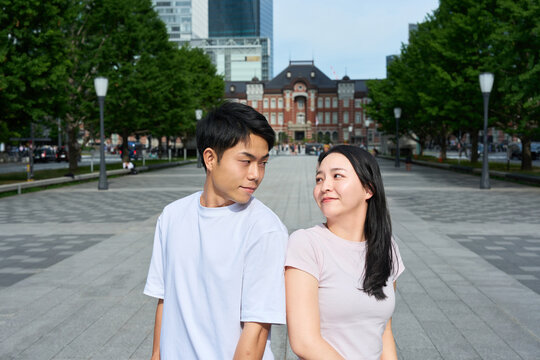 Young Japanese Man and Woman Standing Together on City Street, Gazing at Each Other
