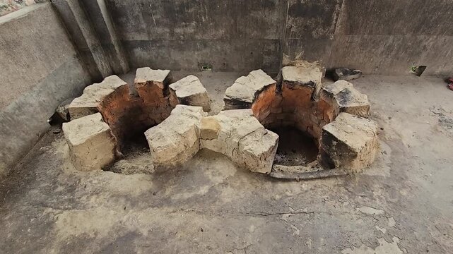 Close-up footage of a traditional double-mouth earthen and brick cooking stove, commonly known as a chulha, built at ground level for wood-fired cooking
