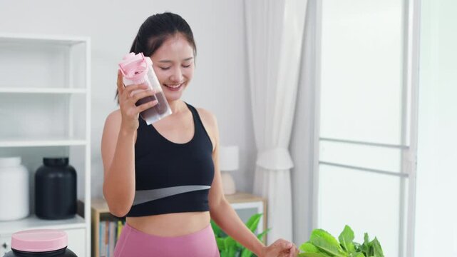 Vibrant Asian fitness vlogger making healthy juice tutorial video in home kitchen. Happy female influencer talking to smartphone camera about nutrition and active lifestyle.