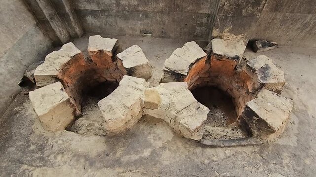 Close-up footage of a traditional double-mouth earthen and brick cooking stove, commonly known as a chulha, built at ground level for wood-fired cooking