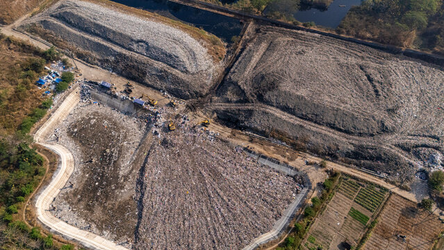 Aerial view of a large landfill site with heavy machinery working on waste piles, surrounded by vegetation and agricultural fields in Klaten, Central Java, Indonesia.