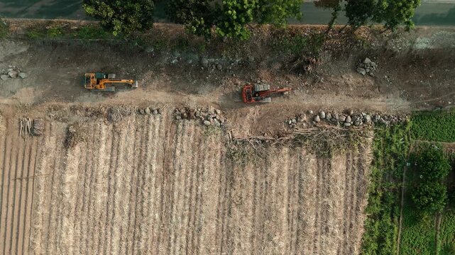 Drone footage showing an aerial view of agricultural fields, including harvested sugarcane and pomelo orange orchards, with heavy machinery parked near a rural road.