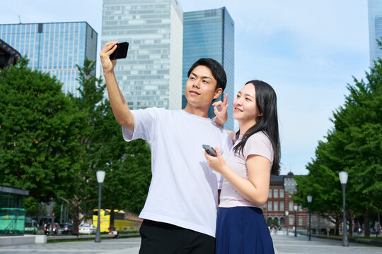 Young Japanese Man and Woman Taking Selfie Together on City Street