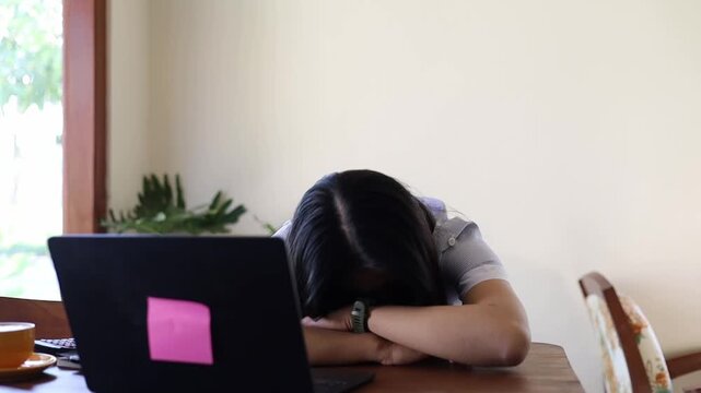 Asian woman sleeping on desk due to overworking and exhausting while working on laptop in cafe