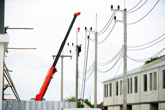 Utility worker repairing electrical wires on pole using crane at construction site