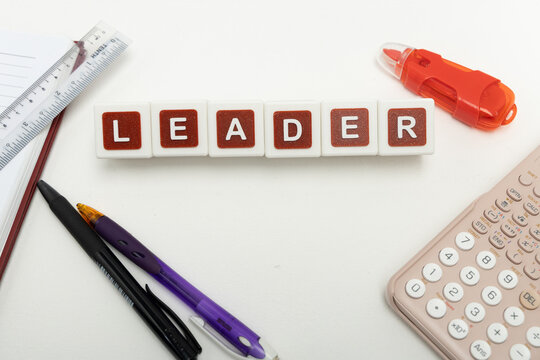 Business organization and administration concept featuring letter blocks spelling &ldquo;LEADER&rdquo; on a clean office desk, surrounded by office stationaries.