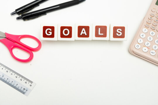 Business organization and administration concept featuring letter blocks spelling &ldquo;GOALS&rdquo; on a clean office desk, surrounded by office stationaries.