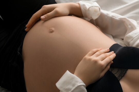Pregnant woman resting hands on belly in white bed