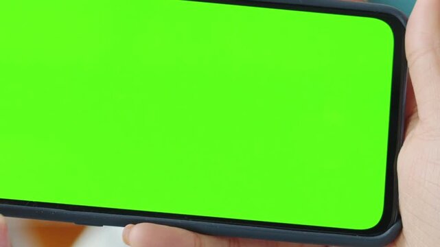 Close up of hands holding a mobile phone with a green screen display for easy video editing and content replacement