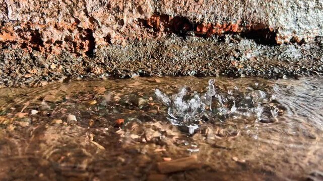 Falling rain disturbs shallow puddle along weathered tunnel edge outdoors