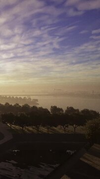 Morning light gently kisses the river and sky, casting a soft glow over distant trees and calm waters. A serene atmosphere envelops the scene, inviting reflection and tranquility.