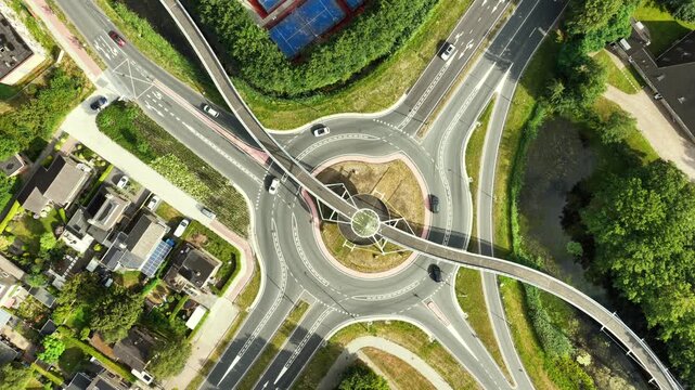 Aerial view of the modern Fietsbrug De Slinger bicycle bridge crossing a busy roundabout with cars and surrounding residential houses in Drachten, Friesland, Netherlands.