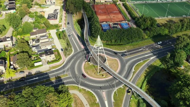 Aerial view of the modern Fietsbrug De Slinger bicycle bridge crossing a roundabout with surrounding roads, green spaces, and residential areas in Drachten, Friesland, Netherlands.