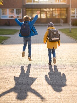 Two young students with backpacks jumping for joy outdoors