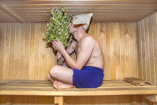 A European man is taking a steam bath, holding a birch whisk.