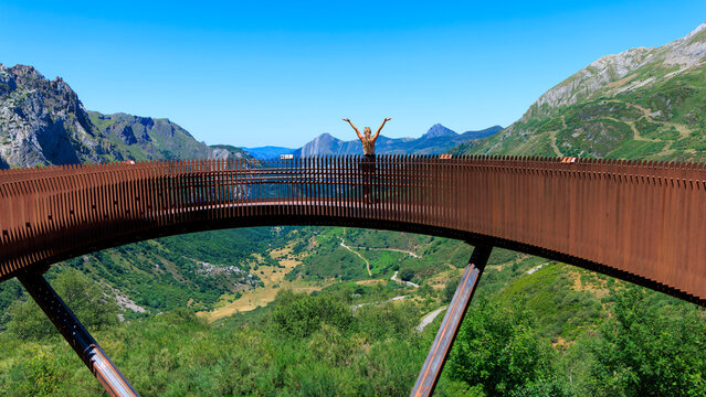 woman standing with open arms on curved viewpoint bridge looking at mountain valley in somiedo asturias spain