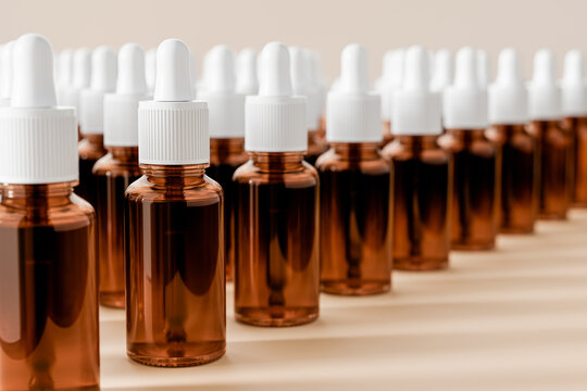 Amber glass dropper bottles filled with cosmetic or pharmaceutical liquid, arranged in rows on a warm neutral background. Skincare, serum, laboratory and beauty product concept.