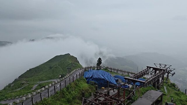 Scenic view of mist-covered green mountains and hills in Darjeeling, West Bengal, India, under an overcast sky. The footage captures the peaceful Himalayan landscape, winding mountain terrain