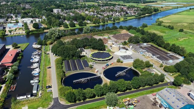 Aerial view of a wastewater treatment plant in Burgum Netherlands with circular treatment tanks, large solar arrays and floating solar panels in a repurposed former settling tank.