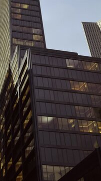 Skyscrapers stand tall against the dusk, their glass facades reflecting the fading light. Office windows glow warmly, hinting at the bustling activity within. The vibrant city feels alive.