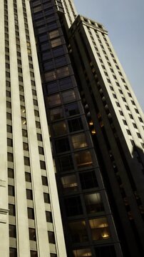 Tall building stretches toward blue sky, showcasing stunning architecture and reflecting sunlight. Windows shine brightly as city life buzzes below, highlighting urban energy and innovation.